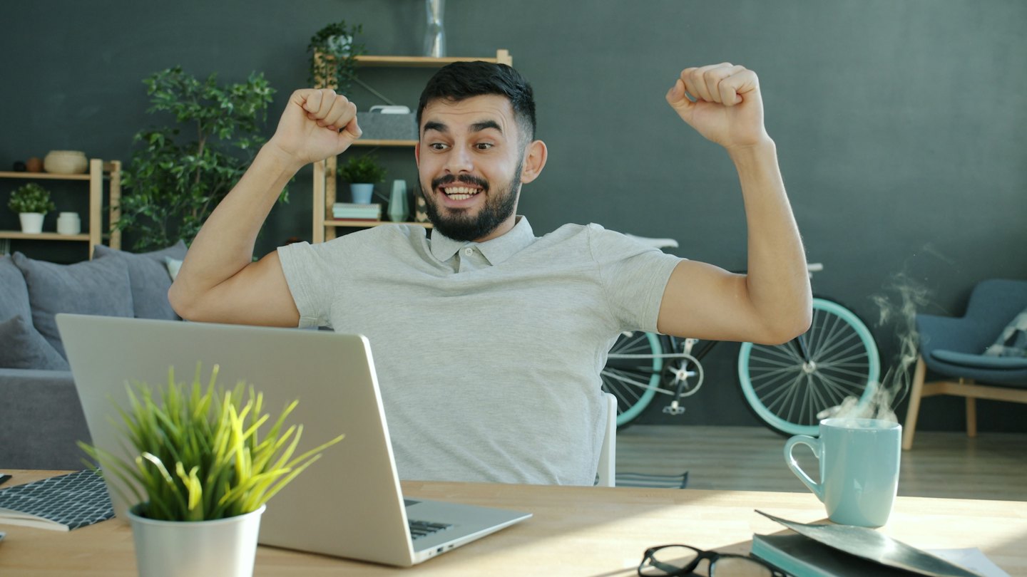 Excited man pumps fists in front of his laptop.